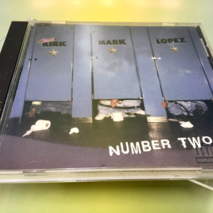 The cover art of "Number Two" by Kirk, Mark, & Lopez. Features the trio in bathroom stalls with their names on them.